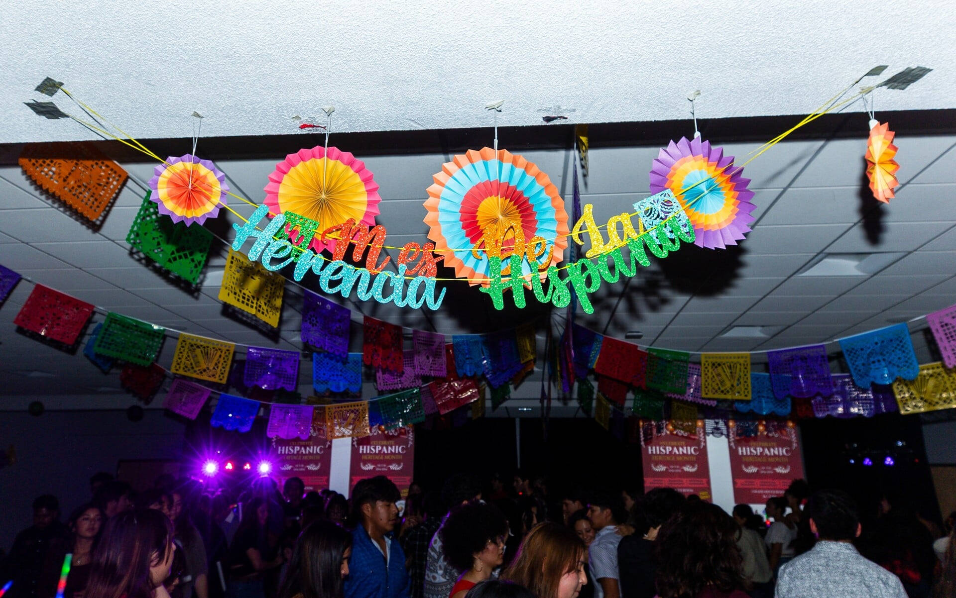 colorful banner with circle fans and flags on the ceiling of the Kirkhof Center for Hispanic Heritage Month, students milling about on the floor for a dance